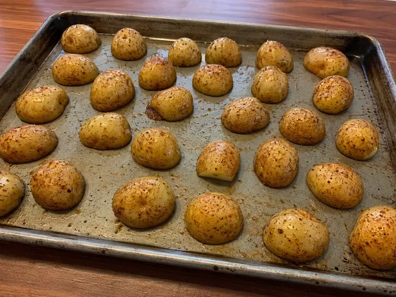 Baby potatoes seasoned with olive oil, paprika, salt, and pepper on a baking sheet before roasting.