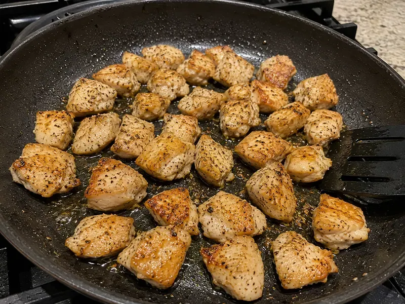 Chicken pieces cooking in a skillet until golden for garlic butter chicken and potatoes.