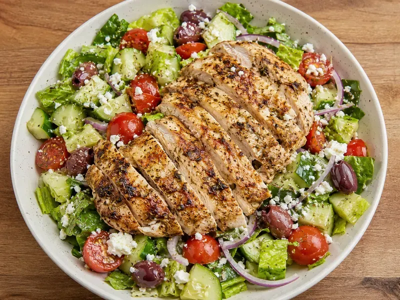 Greek chicken salad with sliced chicken, romaine, cucumber, tomatoes, red onion, olives, feta, and lemon herb dressing.