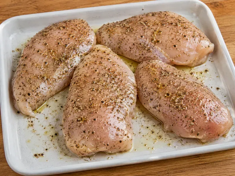 Chicken seasoned with olive oil, oregano, garlic powder, salt, and pepper before cooking.