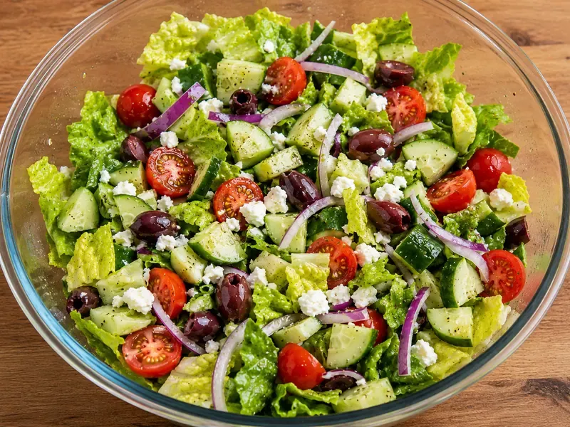 Romaine, cucumber, tomatoes, red onion, olives, and feta prepared in a bowl for Greek chicken salad.