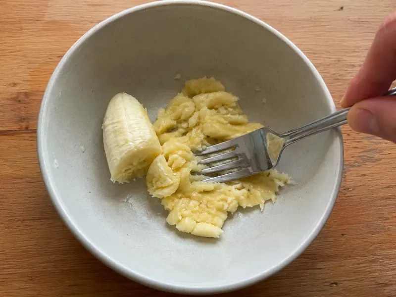 Half a banana mashed in a bowl with a fork.