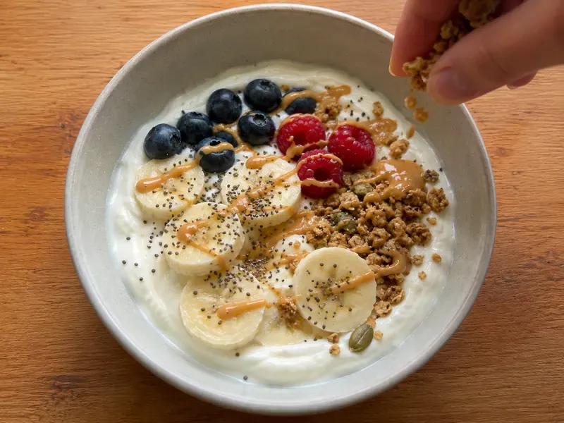 Greek yogurt banana protein bowl topped with banana slices, granola, chia seeds, peanut butter, and berries.