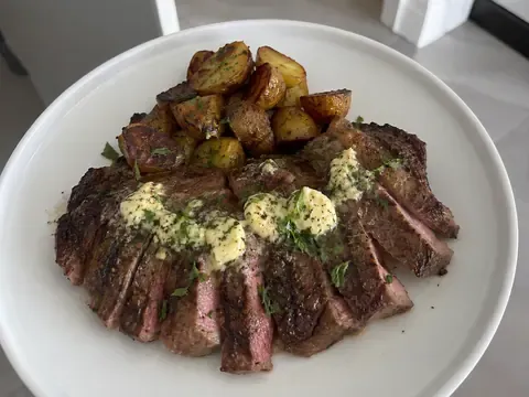 Grilled steak topped with garlic herb butter and served sliced on a board or plate.