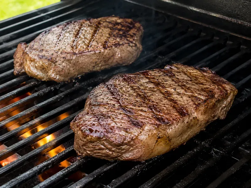 Steaks grilling with visible grill marks forming.