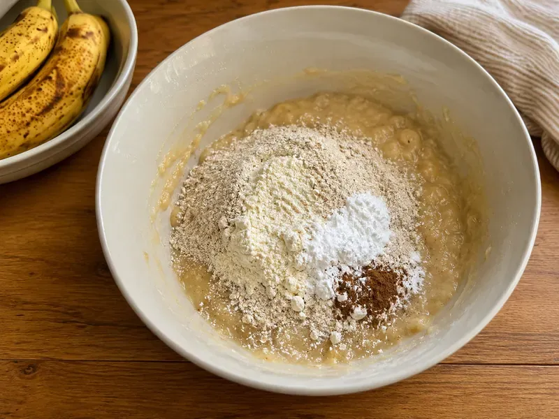 Oat flour, protein powder, cinnamon, baking powder, baking soda, and salt added to banana muffin batter.