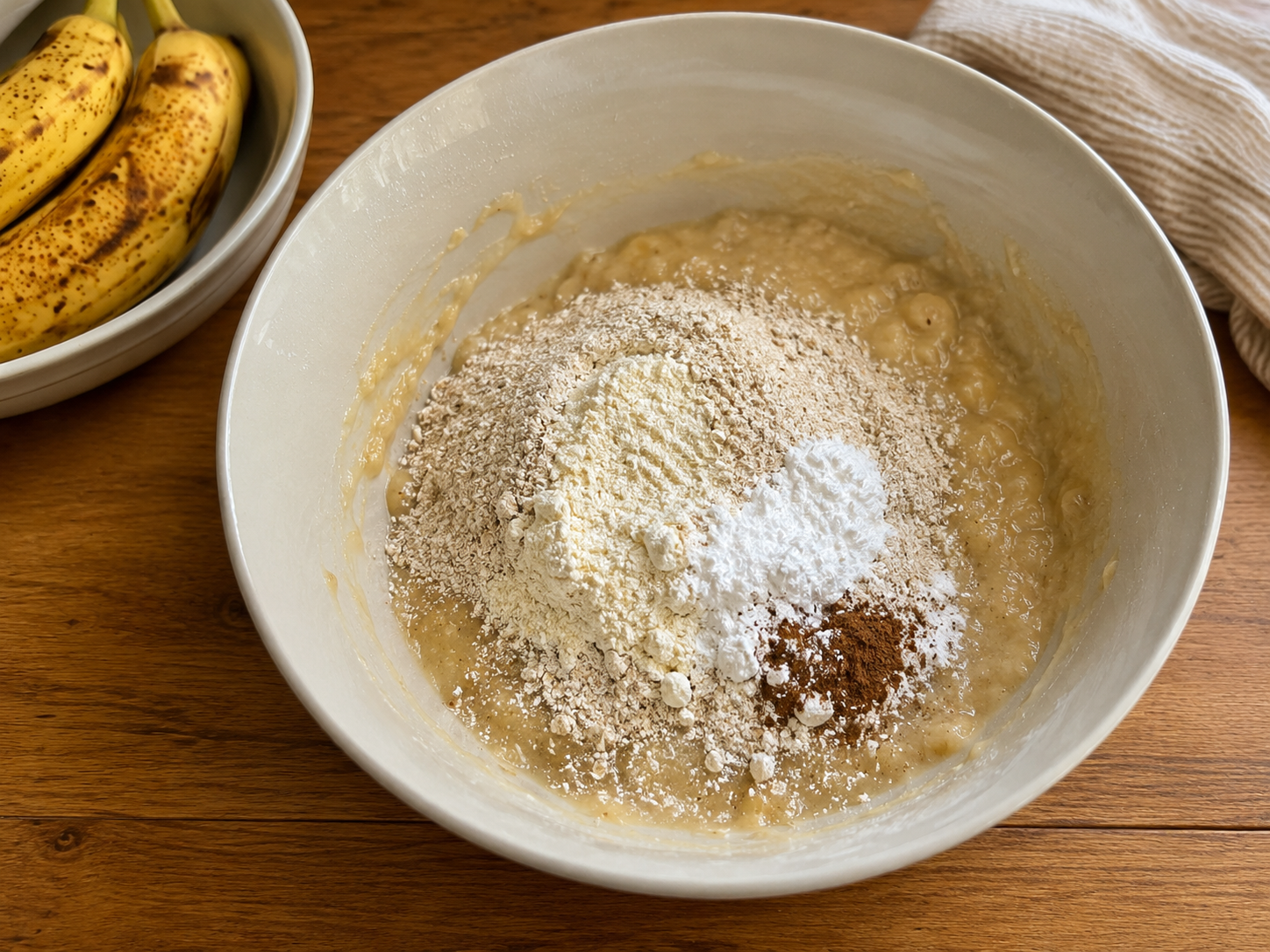 Oat flour, protein powder, cinnamon, baking powder, baking soda, and salt added to banana muffin batter.