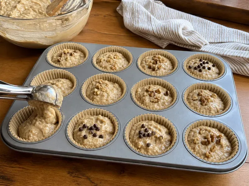 Banana muffin batter divided into a lined muffin pan with optional chocolate chips or walnuts.