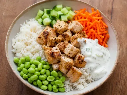 High protein chicken rice bowl with chicken breast, white rice, edamame, cucumber, carrots, and creamy sauce.