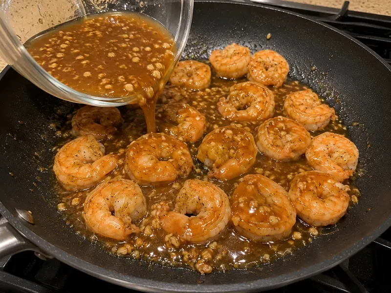 Honey garlic sauce thickening in a skillet and coating cooked shrimp.