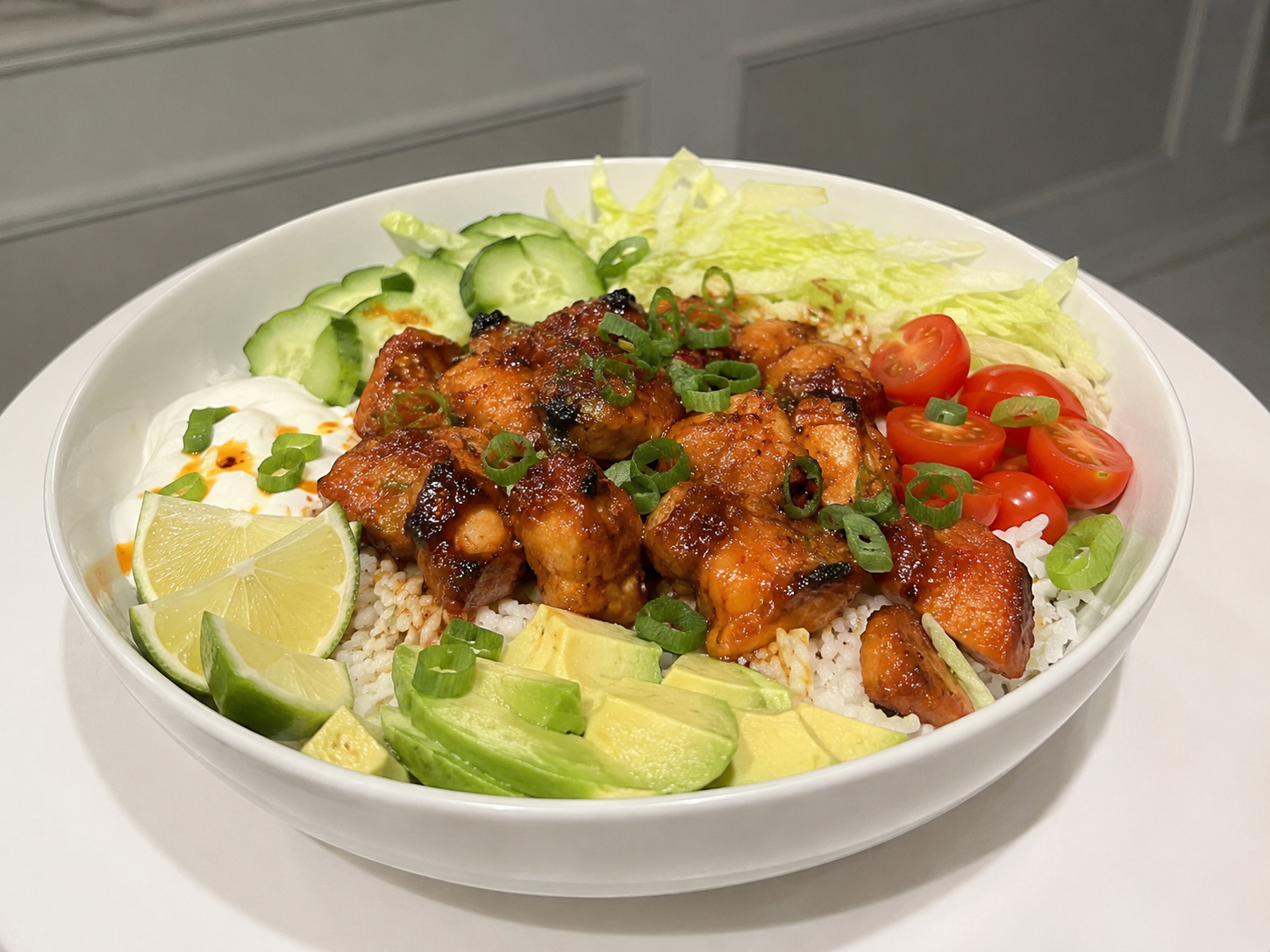 Hot honey chicken bowl with rice, lettuce, cucumber, tomatoes, avocado, green onions, lime, and yogurt.