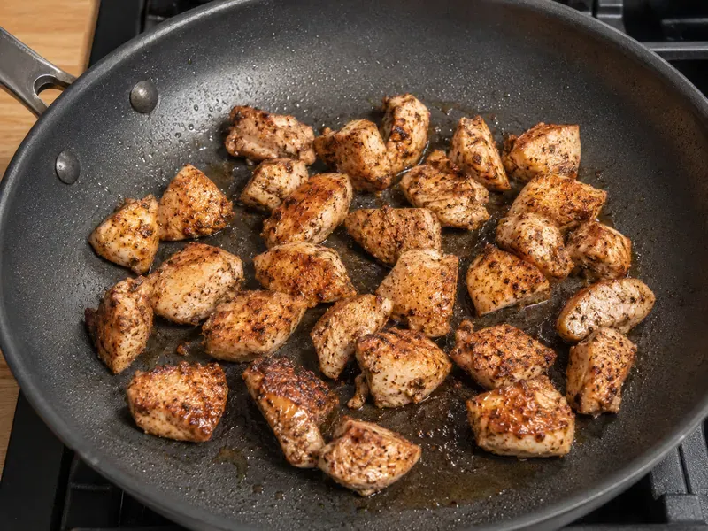 Seasoned chicken pieces cooking in a skillet until browned and cooked through.