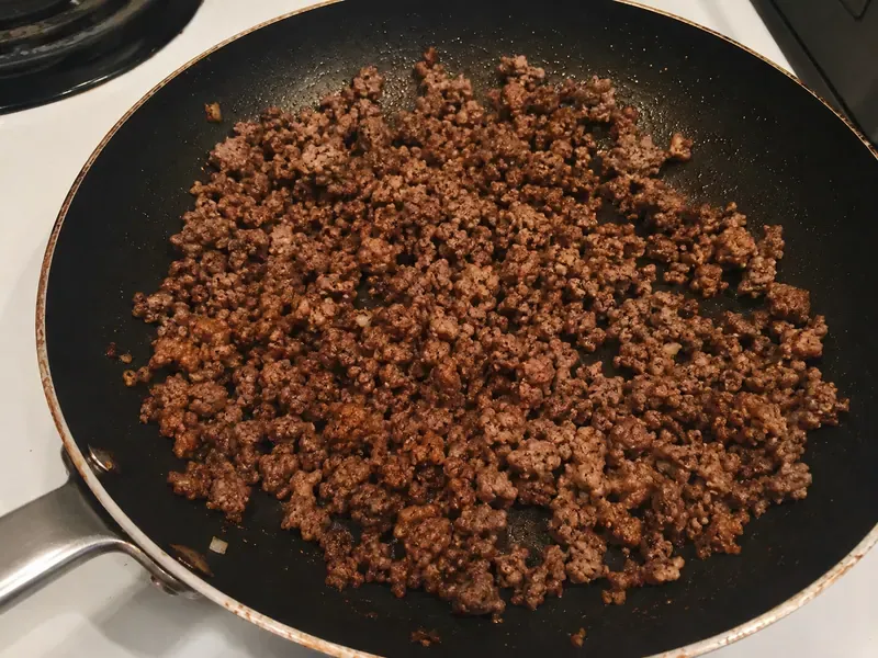 Ground beef cooking in a skillet with garlic and spices for a hot honey cottage cheese beef bowl.