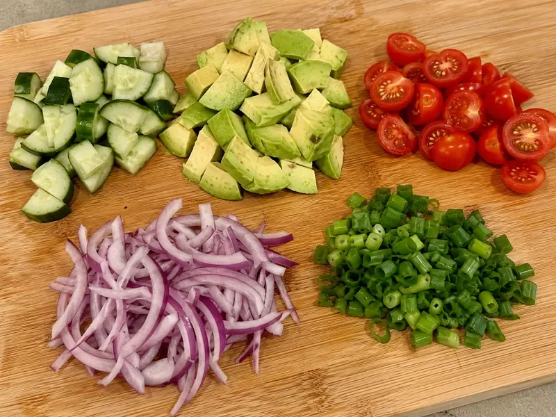 Cucumber, avocado, cherry tomatoes, red onion, and green onions prepared for a cottage cheese beef bowl.