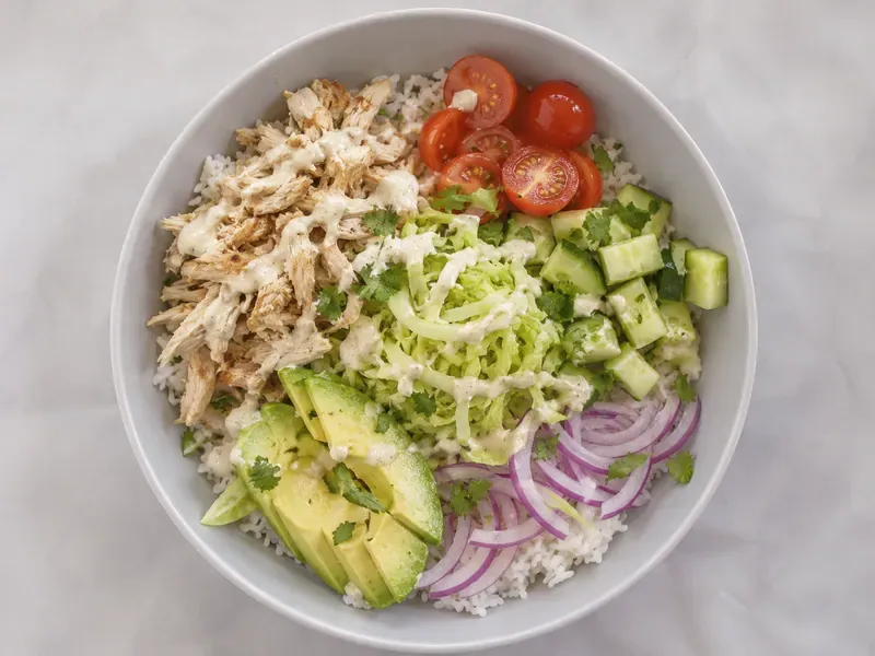 Leftover Rotisserie Chicken Rice Bowls with rice, shredded chicken, cucumber, tomatoes, avocado, herbs, and sauce.