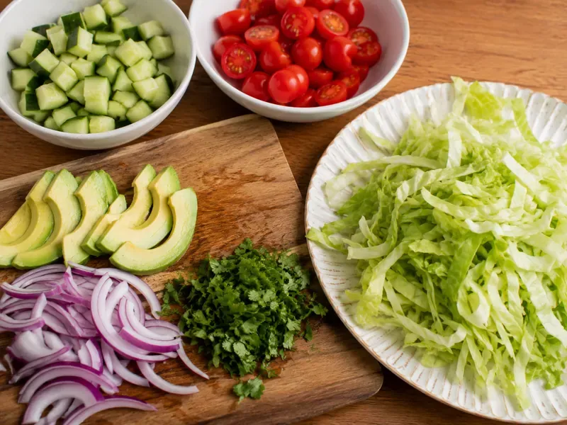 Cucumber, tomatoes, lettuce, avocado, red onion, and herbs prepared for rice bowls.