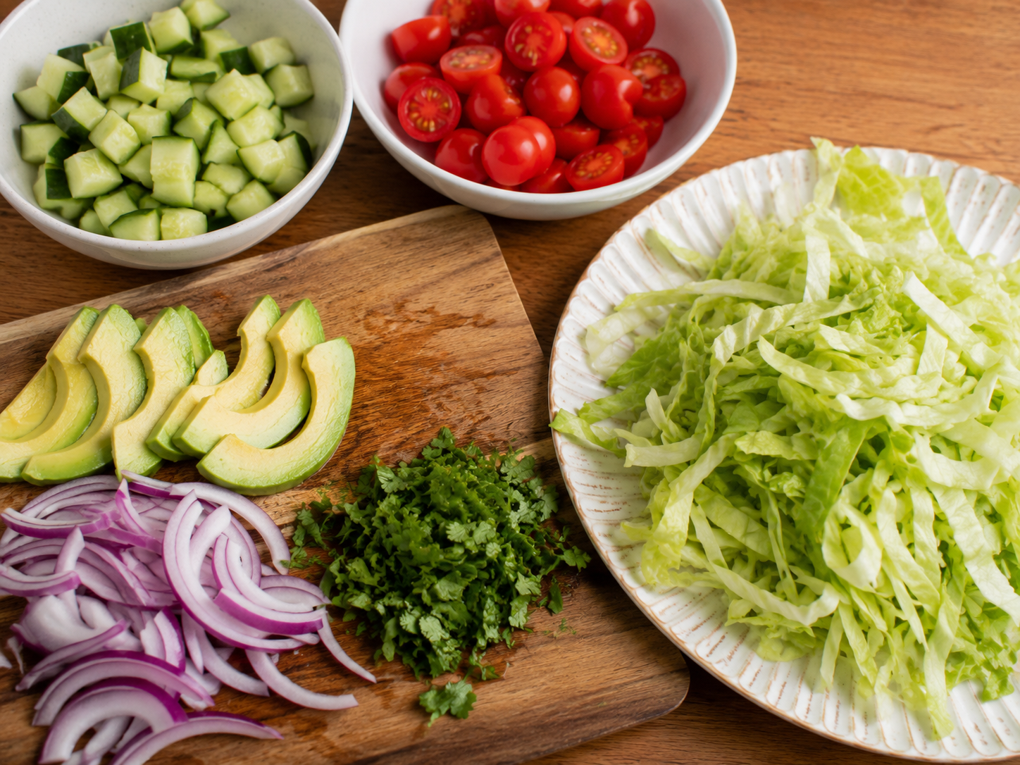 Cucumber, tomatoes, lettuce, avocado, red onion, and herbs prepared for rice bowls.