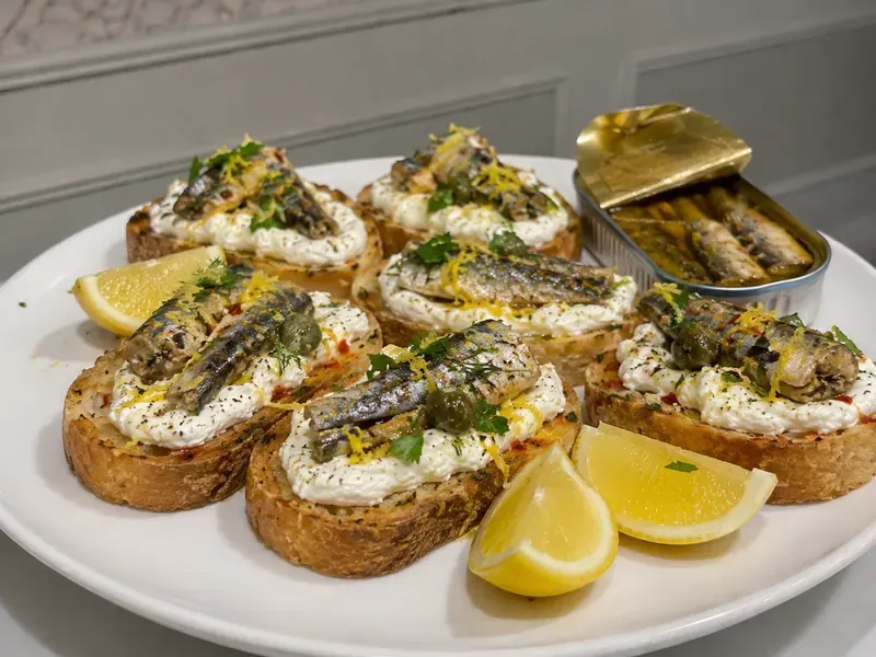 Lemon Ricotta Sardine Toast with creamy ricotta, sardines, herbs, chili flakes, and lemon wedges.