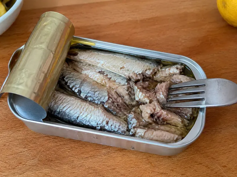 Opened sardine tin with sardines gently separated with a fork.