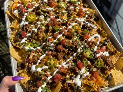 Loaded Pulled Beef Nachos with tortilla chips, shredded beef, melted cheese, beans, jalapeños, salsa, sour cream, and cilantro.