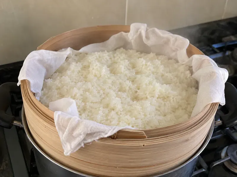 Soaked sticky rice steaming in a lined steamer basket.