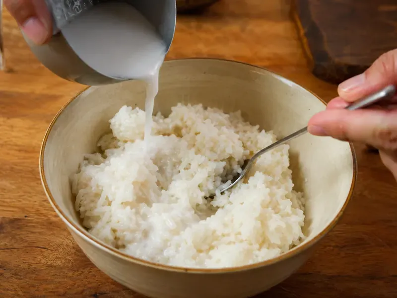 Sweet coconut milk poured over hot sticky rice in a bowl.