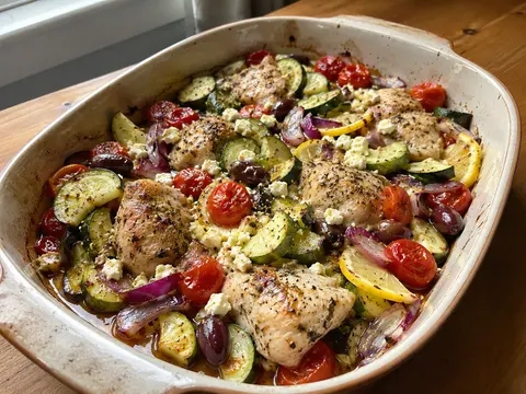 Mediterranean Chicken Zucchini Bake with chicken, zucchini, tomatoes, olives, feta, herbs, and lemon in a baking dish.