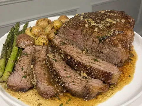 New York Steak Roast Recipe with sliced beef, browned crust, garlic herb butter, herbs, and pan juices.