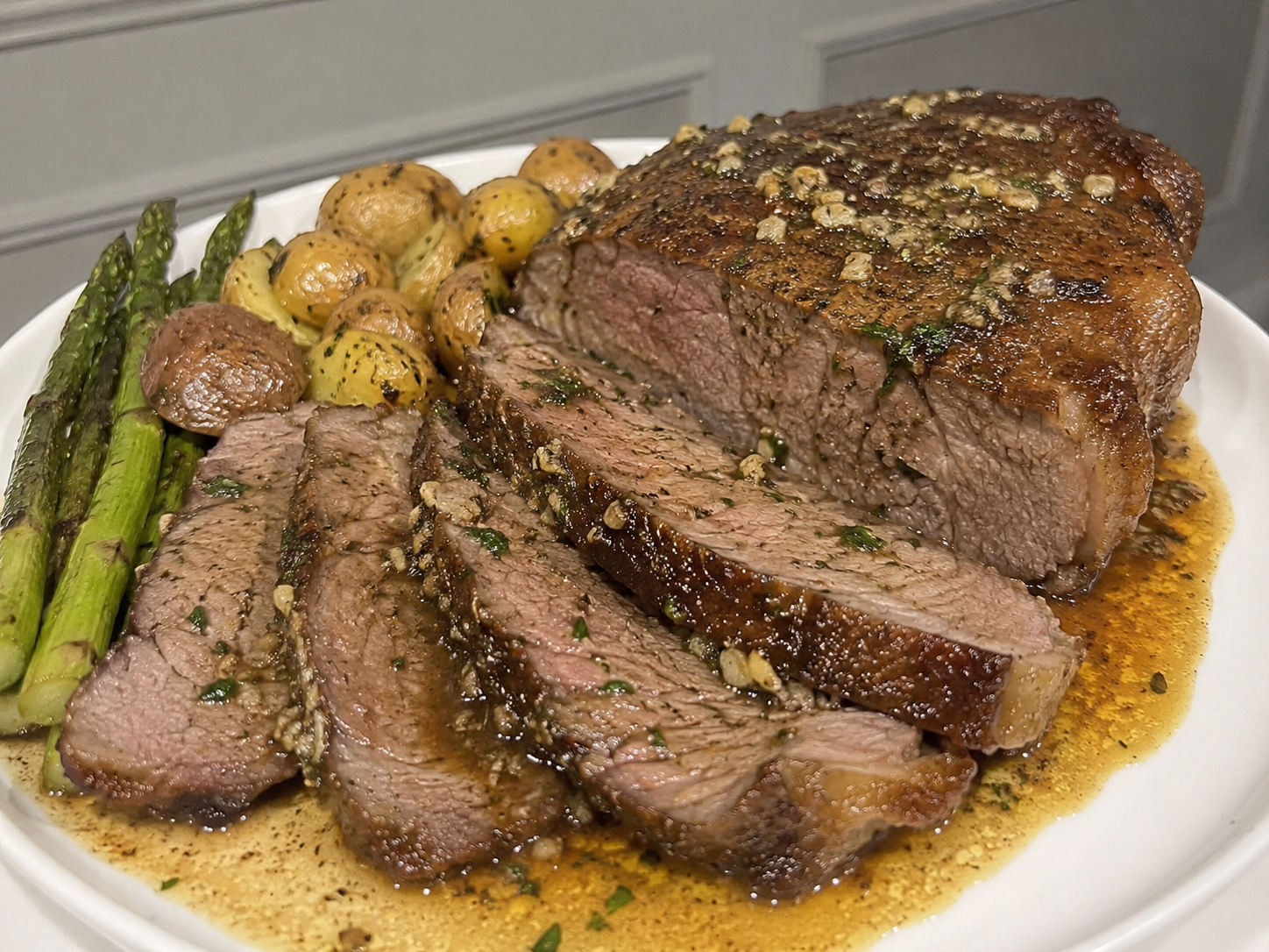 New York Steak Roast Recipe with sliced beef, browned crust, garlic herb butter, herbs, and pan juices.
