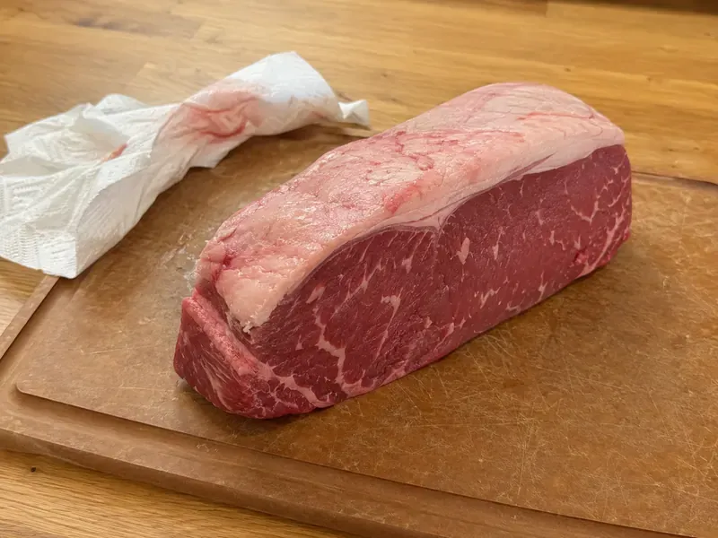 New York strip roast patted dry on a cutting board before seasoning.