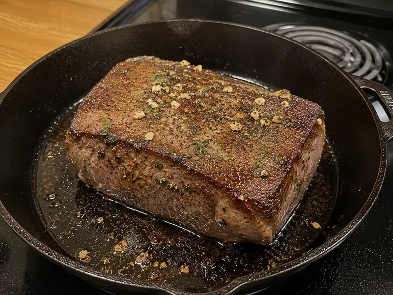 Seasoned New York strip roast seared in a cast iron skillet until browned.