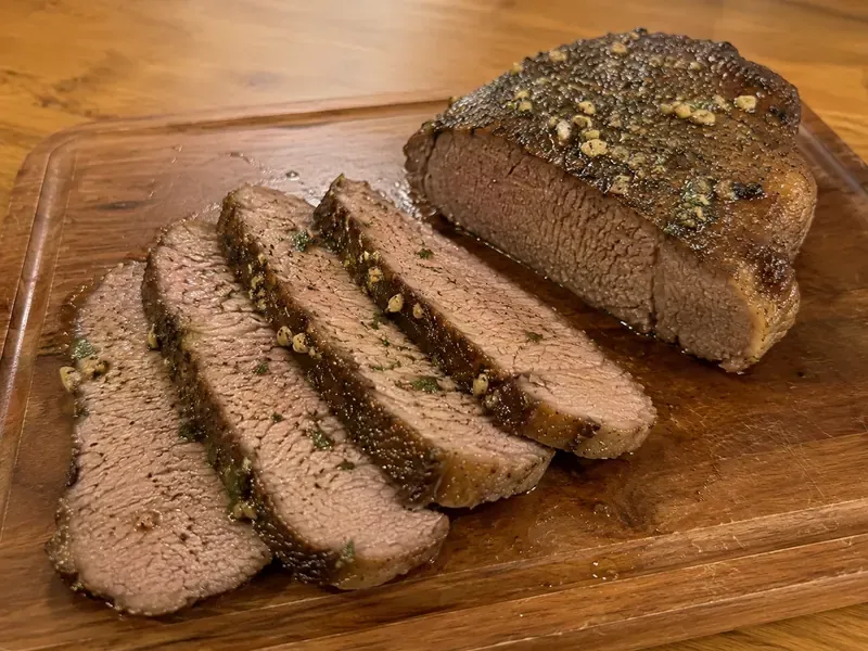 Finished New York steak roast rested and sliced on a cutting board.