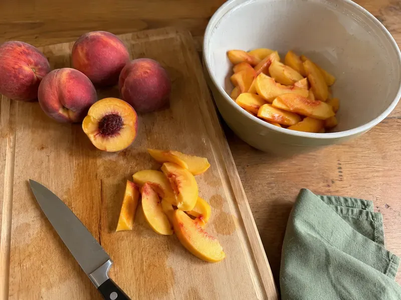Fresh peaches sliced on a cutting board and added to a bowl.