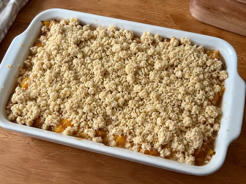 Peach filling in a baking dish covered with crumble topping.