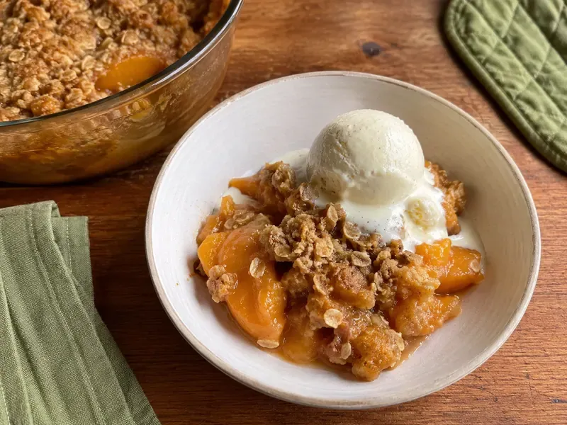 Finished peach crumble served warm with golden topping and juicy peaches.