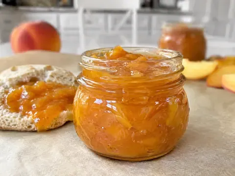 Small-Batch Peach Jam in a glass jar with a spoon and fresh peaches nearby.