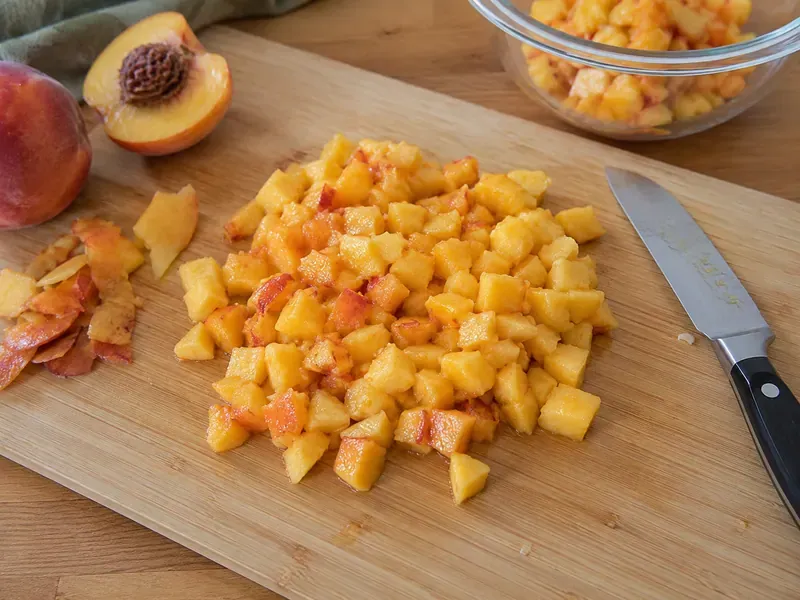 Fresh peaches peeled, pitted, and chopped on a cutting board for peach jam.