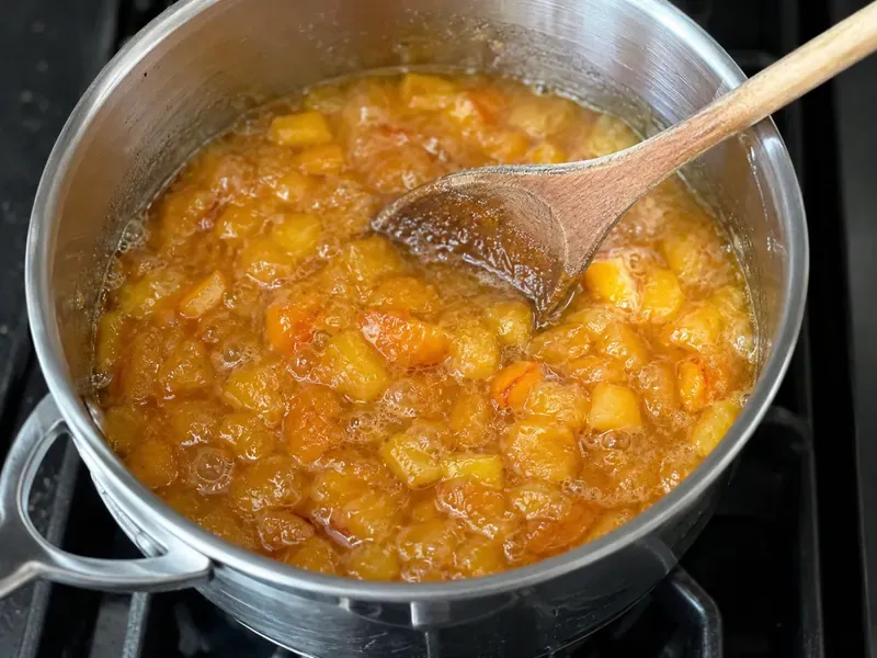 Peach jam simmering in a saucepan until thick and glossy.