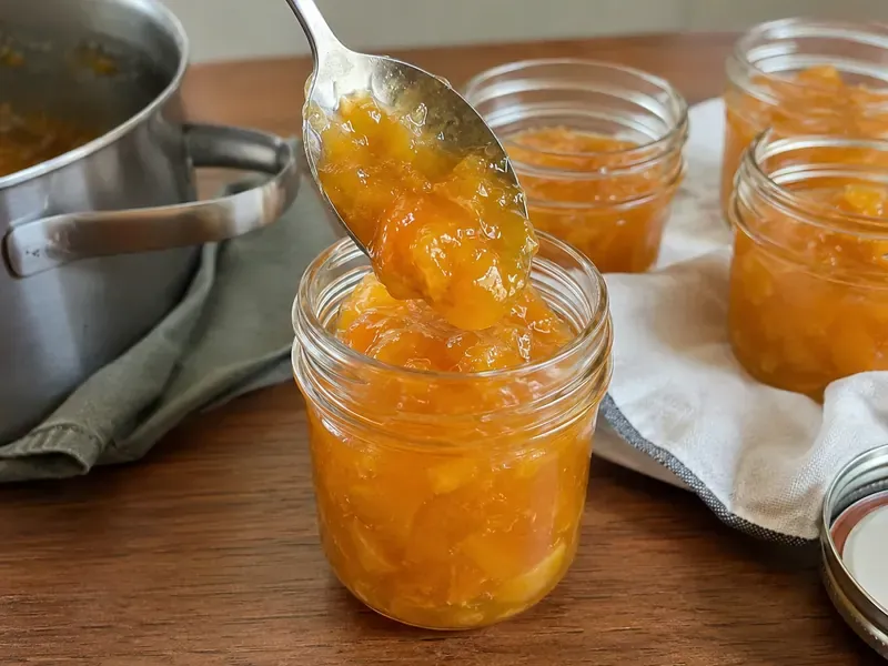 Homemade peach jam spooned into clean small glass jars.