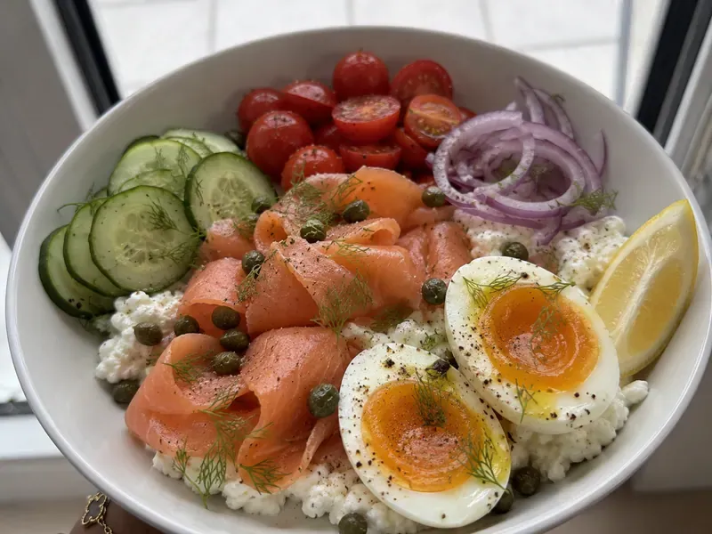 Smoked salmon egg and cottage cheese bowl with jammy eggs, cucumber, tomatoes, red onion, capers, dill, and lemon.