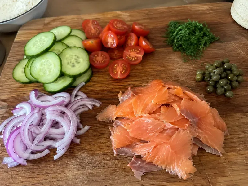 Smoked salmon, cucumber, tomatoes, red onion, dill, and capers prepared for the bowl.
