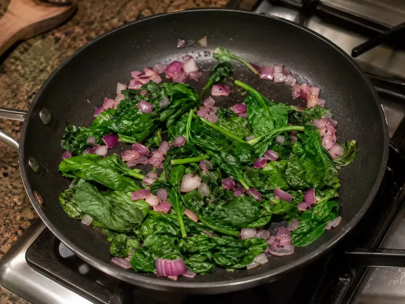Spinach and red onion cooking in a skillet for a breakfast bowl.
