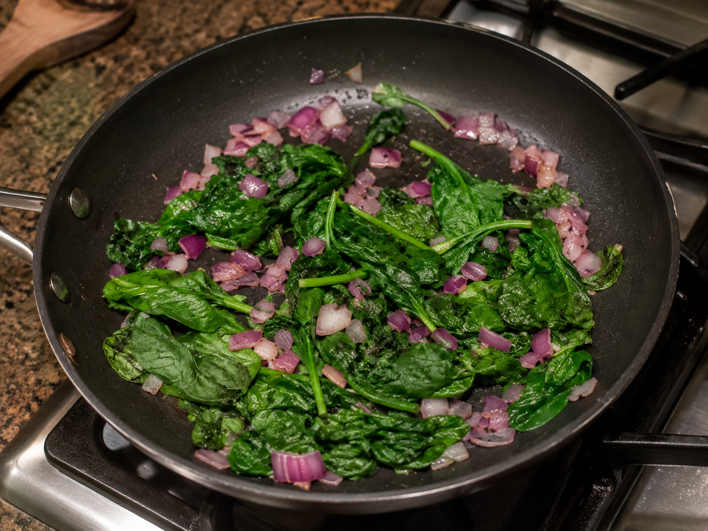 Spinach and red onion cooking in a skillet for a breakfast bowl.