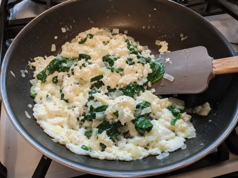 Egg whites gently scrambled with spinach and onion in a skillet.