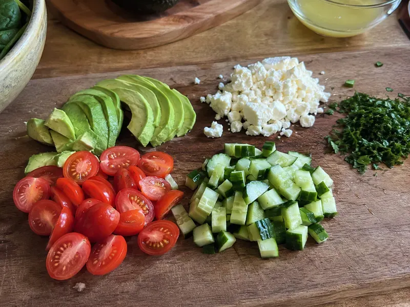 Tomatoes, cucumber, avocado, feta, and herbs prepared for a spinach feta breakfast bowl.
