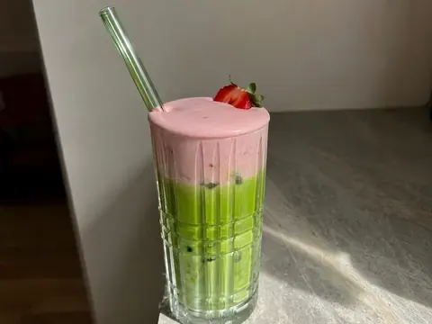 Strawberry Cold Foam Matcha Latte in a clear glass with pink foam, green matcha, milk, and ice.