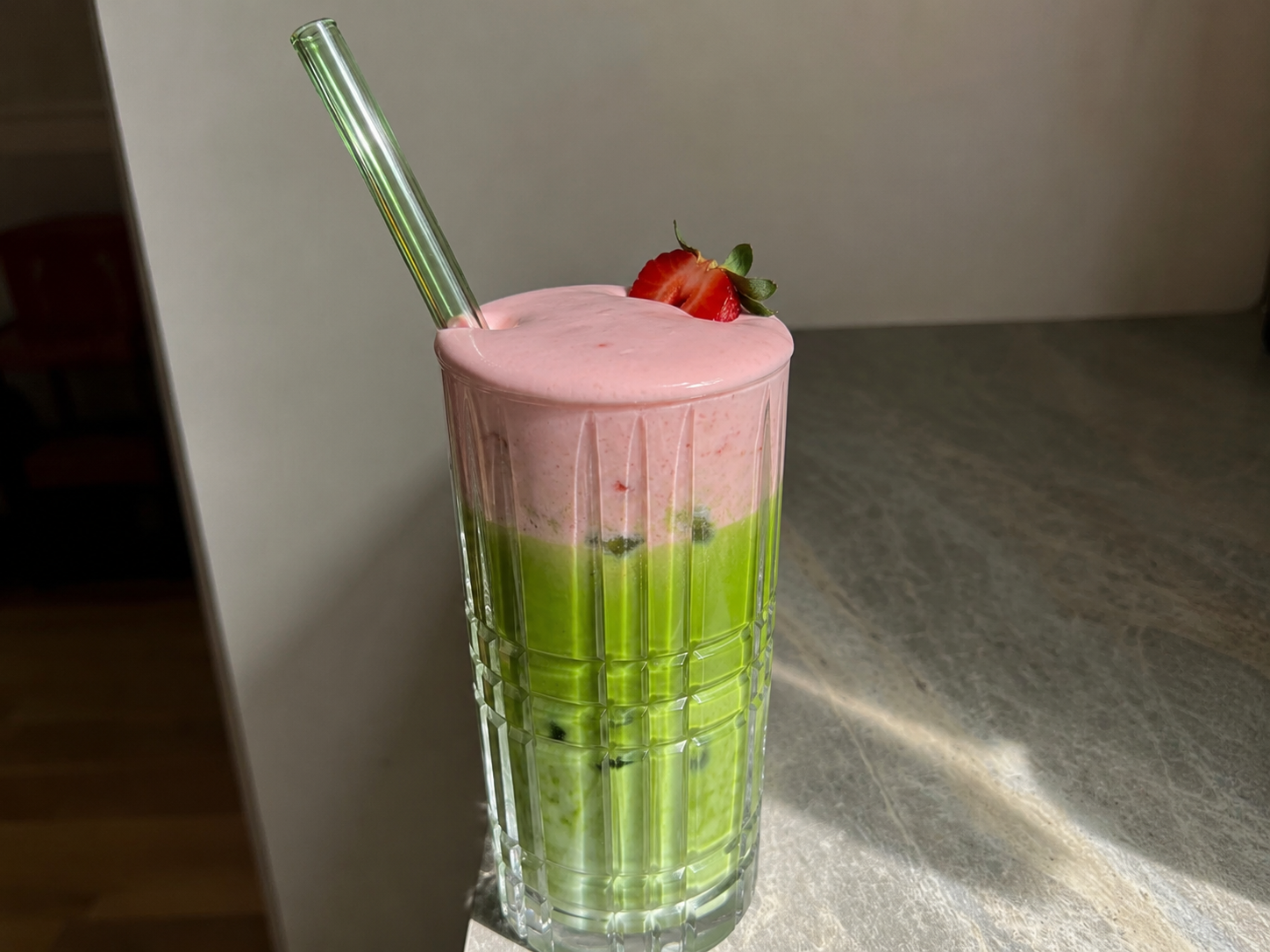 Strawberry Cold Foam Matcha Latte in a clear glass with pink foam, green matcha, milk, and ice.