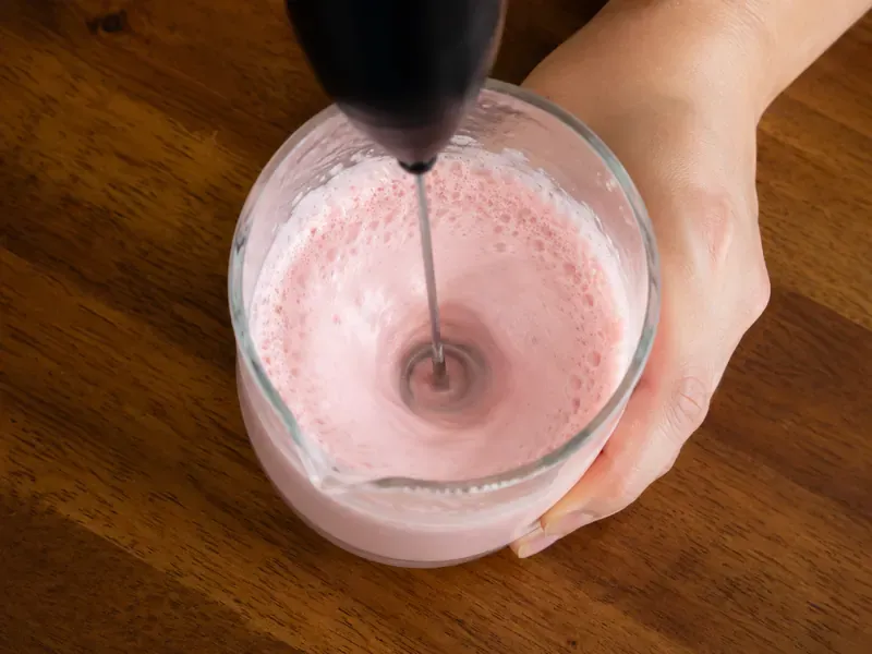 Strawberry cold foam being frothed in a small cup or jar.