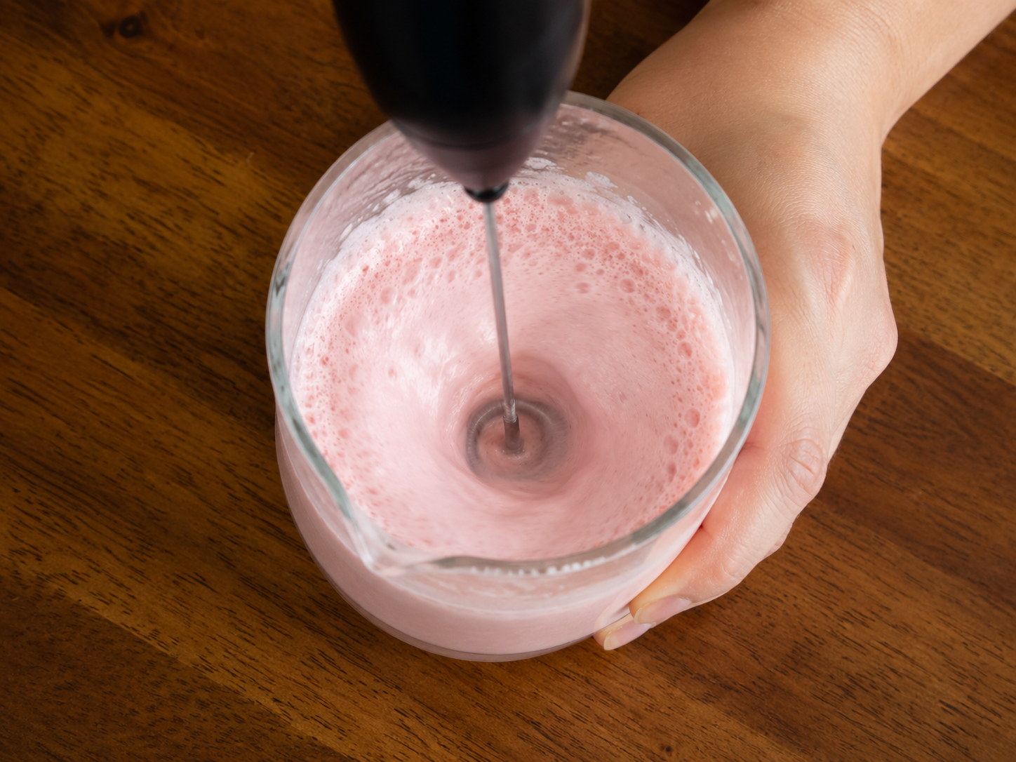 Strawberry cold foam being frothed in a small cup or jar.