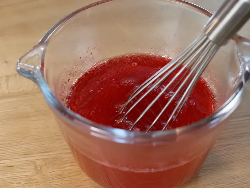 Strawberry gelatin mixed with boiling water in a bowl.
